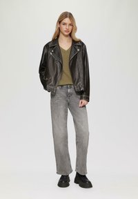 Giubbotto in pelle nera da motociclista con cerniere argento, maglione verde oliva a scollatura a V, jeans grigi a vita alta e stivaletti neri con plateau.