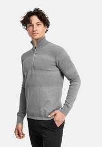 Grauer Reißverschluss-Pullover mit strukturierten Streifen, langen Ärmeln und hohem Kragen. Hat eine taillierte Form und gerippte Bündchen. Wird mit schwarzen Hosen kombiniert.