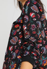Sudadera negra de manga larga con un colorido patrón floral y de paisley, con puños fruncidos y un corte relajado. Textura de tejido impreso.