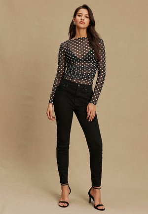 Bluza neagră transparentă cu mâneci lungi și buline albe, design cu adunături; asortată cu blugi negri mulați și sandale negre cu bretele.