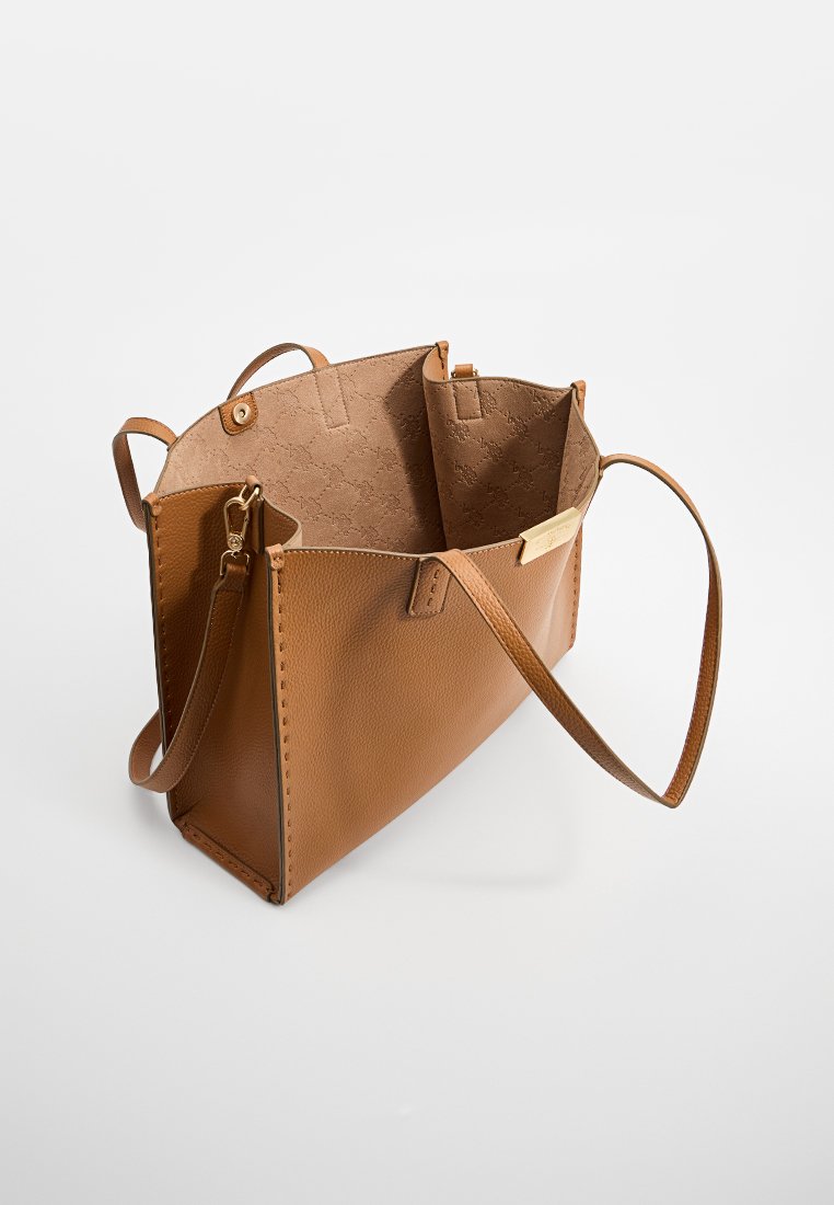 Sac fourre-tout en cuir brun avec une forme structurée, un extérieur lisse et deux poignées. L'intérieur dispose d'une doublure à motifs clairs.