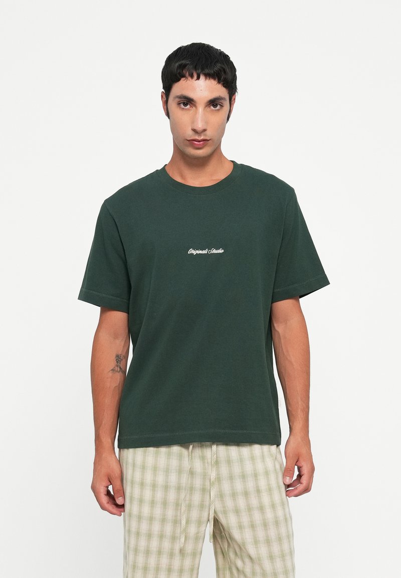 Tricou din bumbac verde închis, cu guler rotund și mâneci scurte; prezintă textul "Original Studio" brodat alb pe piept.