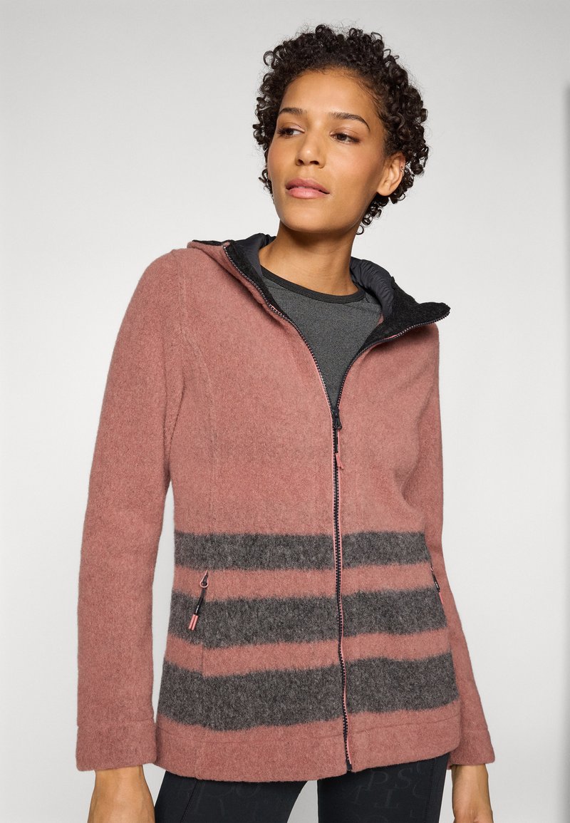 Donna che indossa una giacca in pile con cappuccio a zip, a righe rosa e grigie, che guarda leggermente di lato su uno sfondo chiaro e neutro.