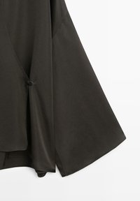 Top in tessuto leggero verde oliva scuro con scollo a V, maniche larghe e chiusura laterale con bottoni. Texture liscia e design minimale.