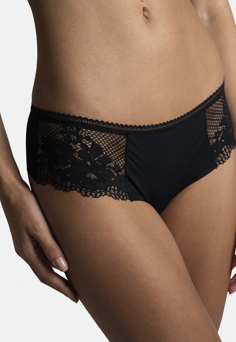 Bas de bikini noir en matériau doux, avec des accents de dentelle sur les côtés dans un motif floral, et un bord festonné.