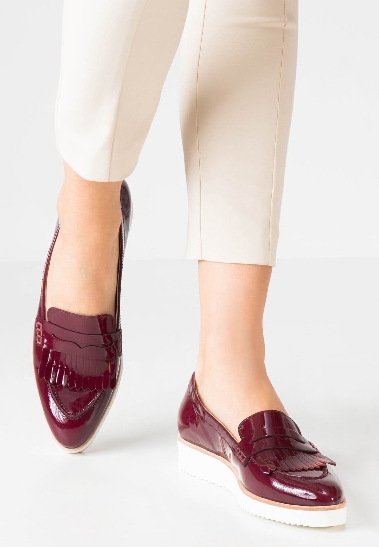 Jambes féminines portant un pantalon crème et des mocassins en cuir bordeaux brillant avec des semelles plates-formes blanches.