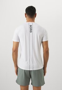 Hvit kortermet treningsskjorte med en vertikal svart "BORG"-logo og kontrastsømmene, kombinert med grå shorts, vist fra baksiden.