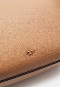 Surface en cuir tanné lisse avec un petit logo gaufré comportant des lettres stylisées et une ligne courbe près du bord inférieur.