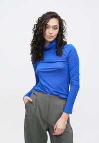 Zils garām piedurknēm ar augstu apkakli džemperis no mīksta, viegla auduma, kombinēts ar pelēkām, ar smalkām svītrām augstiem vidukļa biksēm ar sānu kabatu.