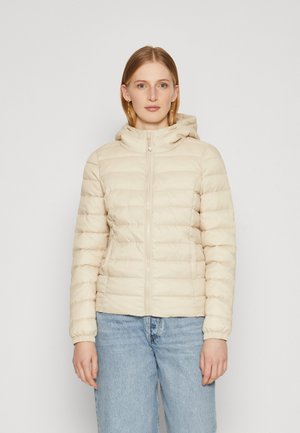 Licht beige pufferjack met een capuchon, met een rits aan de voorkant, ribgebreide manchetten en een gequiltde textuur. Draag het over een blauwe denim broek.