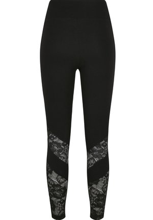 Leggings noirs en tissu lisse et extensible, avec des panneaux en dentelle à motif floral le long des côtés dans un design en chevrons.