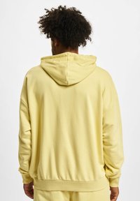 Sweat-shirt à capuche jaune avec une coupe décontractée, des poignets et une ceinture côtelés. Texture lisse sans motifs ni accents visibles.