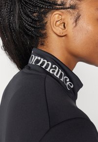 Zwart sporttop met hoge kraag met zilveren "performance" tekst, gemaakt van een gladde, rekbare stof, met een aangesloten ontwerp.