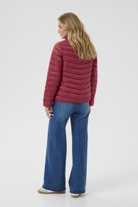 Rdeča, quiltana puffer jakna s chevron vzorcem, visokim ovratnikom in dolgimi rokavi, oblečena čez široke modre jeans hlače.