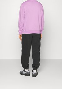 Felpa lilla con polsini e orlo a coste, abbinata a pantaloni jogger neri e sneakers grigie con dettagli neri e logo.