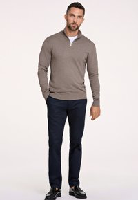 Brauner, Pullover mit Reißverschluss und passgenauer Schnitt, kombiniert mit dunkelblauen Hosen und schwarzen Schuhen. Weicher Stoff mit gerippten Bündchen und Saum.