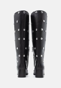 Μαύρες μπότες μέχρι το γόνατο από λείο δέρμα, με ασημένια τρουκς και στιβαρό τακούνι τύπου block. Κλείσιμο στο πλάι με φερμουάρ και ραβδωτές λεπτομέρειες.