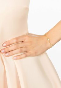 Arany karkötő virágos díszítéssel, három dekoratív virággal. Finom láncfrastruktúra, amely egy puha, világos szöveten nyugvó kézen viselhető.