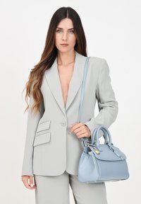 Blazer su misura grigio chiaro con rever a apertura, spalle strutturate, abbinato a una borsa in pelle azzurro chiaro con manici superiori e hardware dorato.