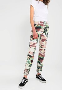 Mönstrade, figursydda byxor med blommönster och camouflage i nyanser av grönt, rosa och kräm. Har dragkedja och femficksdesign.