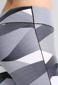 Leggings ajustados con un patrón geométrico en blanco y negro, que presentan líneas y texturas distintas, fabricados con un tejido elástico y suave.
