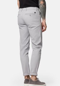 Jasnoszare chinos o dopasowanym kroju, z mankietami, tylnymi kieszeniami i subtelnym brandingiem. Wykonane z miękkiego, gładkiego materiału bawełnianego.