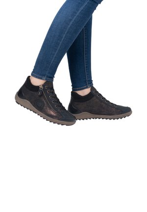 Chaussures décontractées noires avec un design bronze texturé, des zips, des œillets dorés et une semelle en caoutchouc. Assorties avec un jean skinny bleu.
