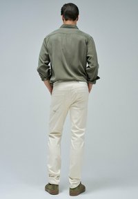 Chinos beige claros con un corte slim, bolsillos traseros y un detalle de costura sutil, combinados con una camisa de botones verde oliva.