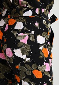 Tissu noir couvert de motifs floraux multicolores, comprenant des roses orange, roses et blanches avec des feuilles vertes ; inclut une poche latérale.