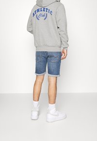 Šedá mikina s modrým potiskem "ATHLETIC Club" na zádech, doplněná džínovými �šortkami a bílými vysokými teniskami. Texturovaná látka a ohrnuté manžety.