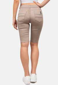 Bermudas en denim beige, taille mi-haute, poches arrière avec couture décorative, portées avec des baskets blanches. Texture lisse, coupe ajustée.