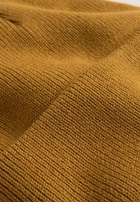 Knitted fabric in a rich mustard color, featuring a textured pattern with visible, even stitches and slight stretch along the surface.