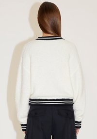 Weißer, flauschiger Pullover mit schwarz-weißen, gestreiften Rippbündchen und -saum. Mit herunterhängenden Schultern und einem Rundhalsausschnitt. Weicher Stoff.