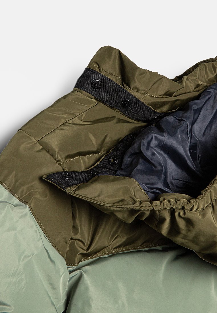 Veste rembourrée avec une couche extérieure vert olive, une doublure navy, des boutons pression et des poignets élastiques. Présente une texture lisse et un design matelassé.