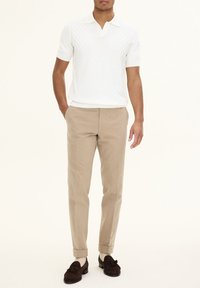 Kortärmad vit stickad polo med diamantmönster, i kombination med beige skräddarsydda byxor och bruna mockaloafers med tofsdetaljer.