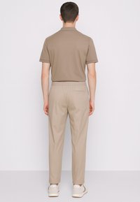 Polo beige con maniche corte e rifiniture a contrasto, abbinato a pantaloni beige con vita elasticizzata. È visibile il retro del modello.