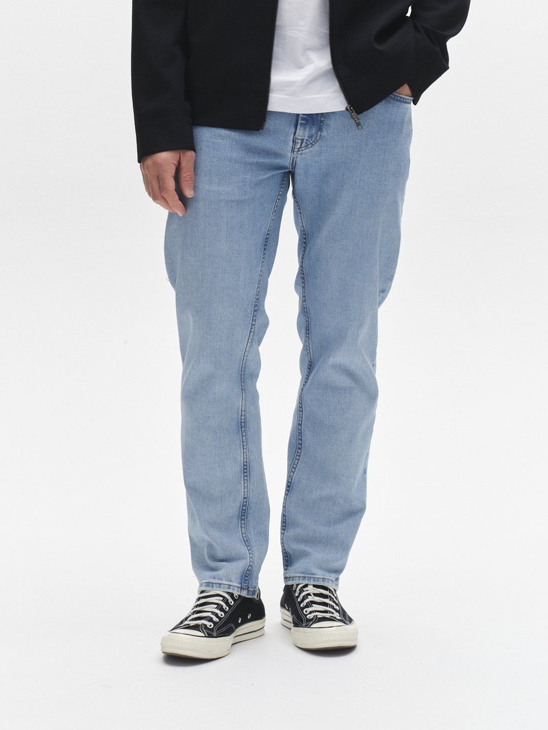 Lyseblå jeans i denim med rette ben, med synlige sømmer og sidelommer. Kombinert med svarte og hvite tøysko.