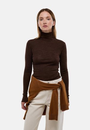 Un haut col roulé marron en matière douce, associé à un pantalon taille haute de couleur claire, avec un pull marron noué à la taille.