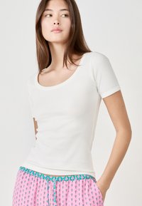 T-shirt bianco a coste, aderente, con scollatura a girocollo e maniche corte, abbinato a pantaloni da pigiama rosa a fantasia con vita turchese.