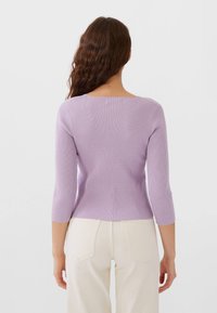 Fialový žebrovaný top s kulatým výstřihem, tříčtvrtečními rukávy a přiléhavým střihem. Nošený s kalhotami světle barvy.