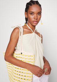 Saco de croché com um padrão em rede em rosa pastel e amarelo. Apresenta uma alça resistente e um acabamento texturizado, destacando o seu aspeto artesanal.