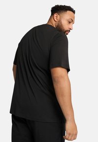 Tricou negru cu mâneci scurte, decolteu rotund și croială lejeră. Textură netedă, fără modele vizibile sau detalii din metal.