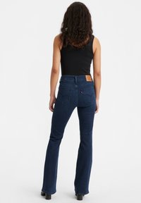 Donkerblauwe flared jeans met een hoge taille, een leren achterpatch en twee achterzakken. De stof lijkt denim met een gladde textuur.