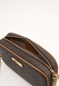 Piccola borsa a tracolla in pelle marrone con cerniera dorata e tracolla a catena, parzialmente aperta che mostra la fodera interna in tessuto.