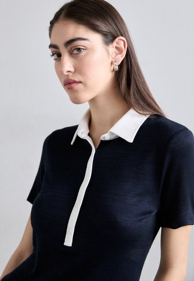 Navy knit polo shirt with a white collared neckline and short sleeves; features button closure and a textured fabric.