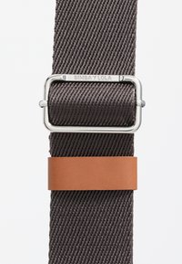 Woven fabricowy pasek w ciemnym brązie z gładkim, brązowym skórzanym akcentem. Charakteryzuje się prostokątną, srebrną metalową klamrą.