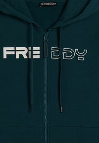 Felpa con zip di colore teal, dalla vestibilità aderente, con la scritta bianca "FREDDY" in evidenza sul petto e una zip frontale con elementi in metallo nero.