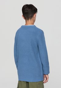 Niebieski sweter dzianinowy z okrągłym dekoltem, długimi rękawami i ściągaczem. Teksturowany materiał charakteryzuje się luźnym krojem. Widok z tyłu.