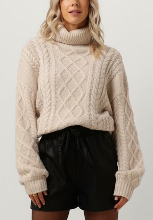 Cream-colored knitted sweater featuring a chunky turtleneck, cable knit patterns, and ribbed cuffs, paired with high-waisted black shorts.