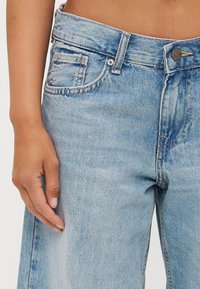 Jeans de ganga azul claro com cintura alta, cinco bolsos e fecho de botão. Apresenta um desbotamento subtil e um design de perna reta.